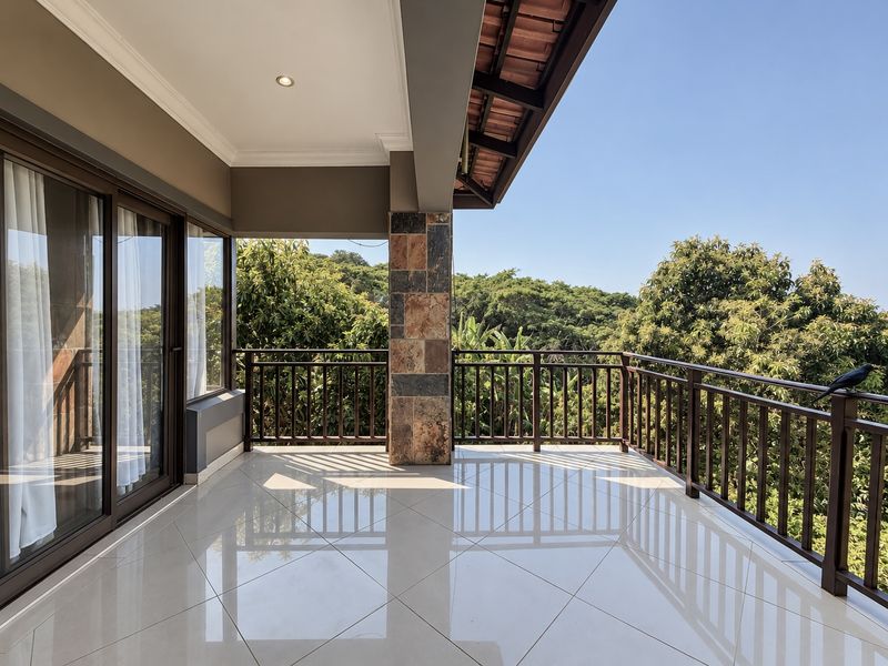 A spacious covered balcony featuring polished tile flooring, a stone-clad support pillar, and a wooden railing, offering scenic views of the surrounding greenery.