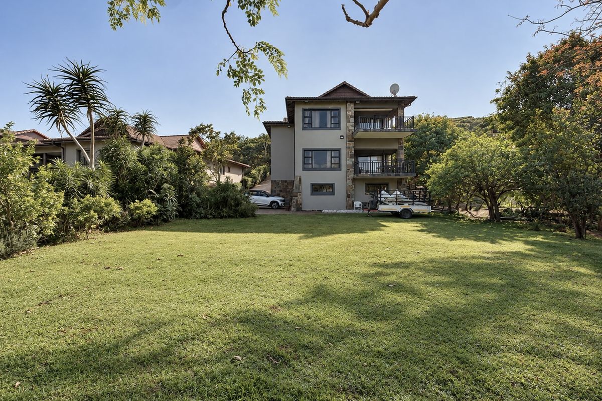 A rear view of a multi-story house featuring stone cladding, multiple balconies, and a spacious, well-maintained lawn area.