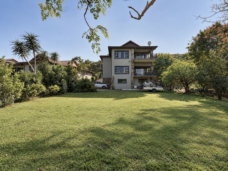 A rear view of a multi-story house featuring stone cladding, multiple balconies, and a spacious, well-maintained lawn area.
