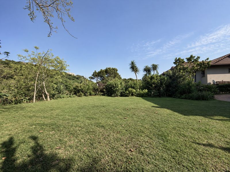 A well-maintained, spacious garden area featuring a lush green lawn surrounded by mature trees and established landscaping.