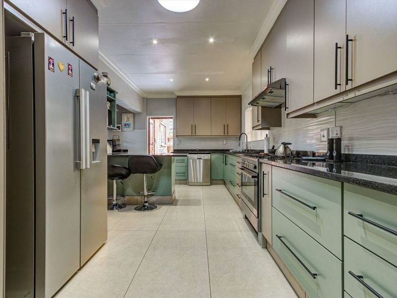 Modern kitchen featuring two-tone cabinetry, granite countertops, stainless steel appliances, and tiled flooring with recessed lighting.