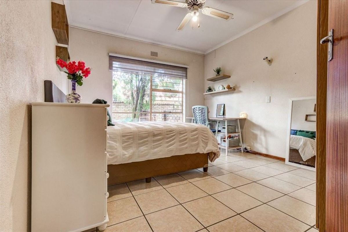 A well-lit bedroom featuring neutral tiled flooring, a ceiling fan, and built-in wall shelving, offering a functional and comfortable living space.
