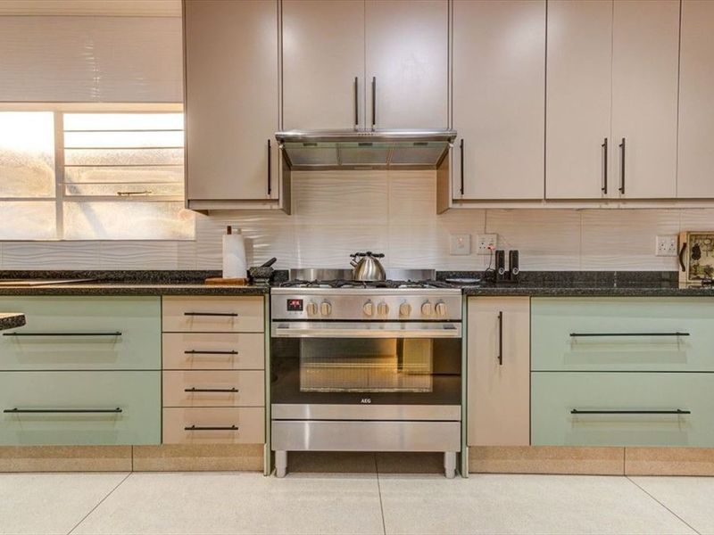 A well-maintained kitchen featuring two-tone cabinetry, granite countertops, and a stainless steel gas stove with an integrated extractor fan.