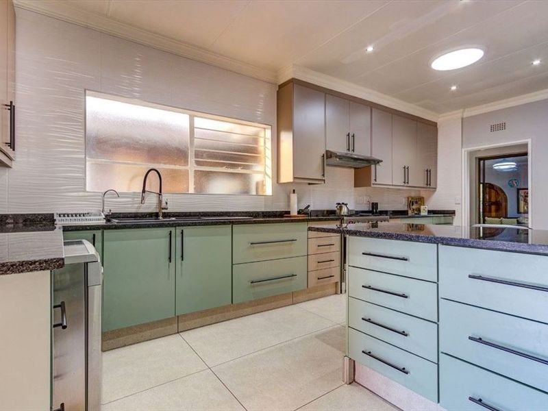 Modern kitchen featuring granite countertops, ample built-in cabinetry, a stainless steel sink, and a bright skylight, offering a functional and well-maintained cooking space.