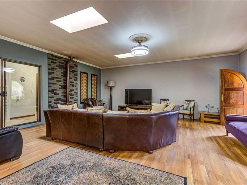 Spacious living room featuring laminate flooring, a stone accent wall, dual skylights, and a ceiling fan, with direct access to the kitchen area.