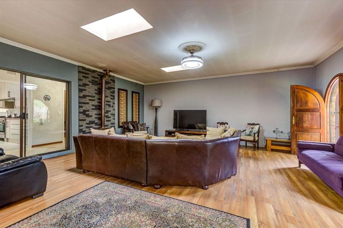 Spacious living room featuring laminate flooring, a stone accent wall, dual skylights, and a ceiling fan, with direct access to the kitchen area.