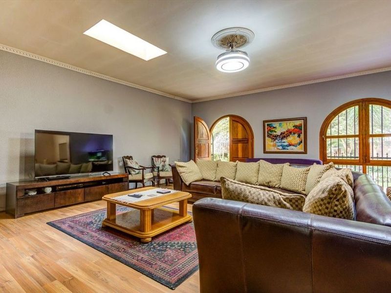 Spacious living room featuring laminate flooring, a skylight, and distinctive arched wooden doors and windows providing natural light.