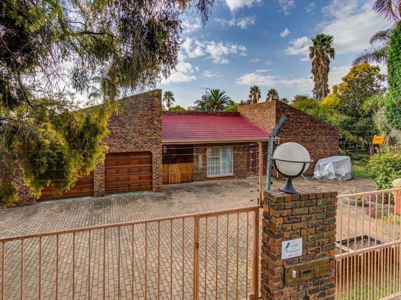 Front view of a face brick house featuring a double garage, paved driveway, and secure gated entrance with established garden surroundings.