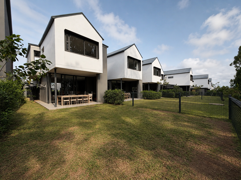 Rear view of modern residential units featuring white facades, metal roofs, covered patios, and private fenced garden spaces.