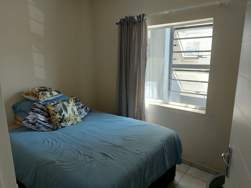 A functional bedroom featuring tiled flooring and a window fitted with security burglar bars, providing natural light and ventilation.