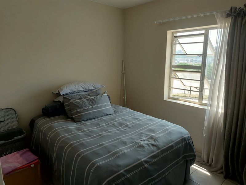 A functional bedroom featuring tiled flooring and a window fitted with security bars, offering natural light and a view of the surrounding area.