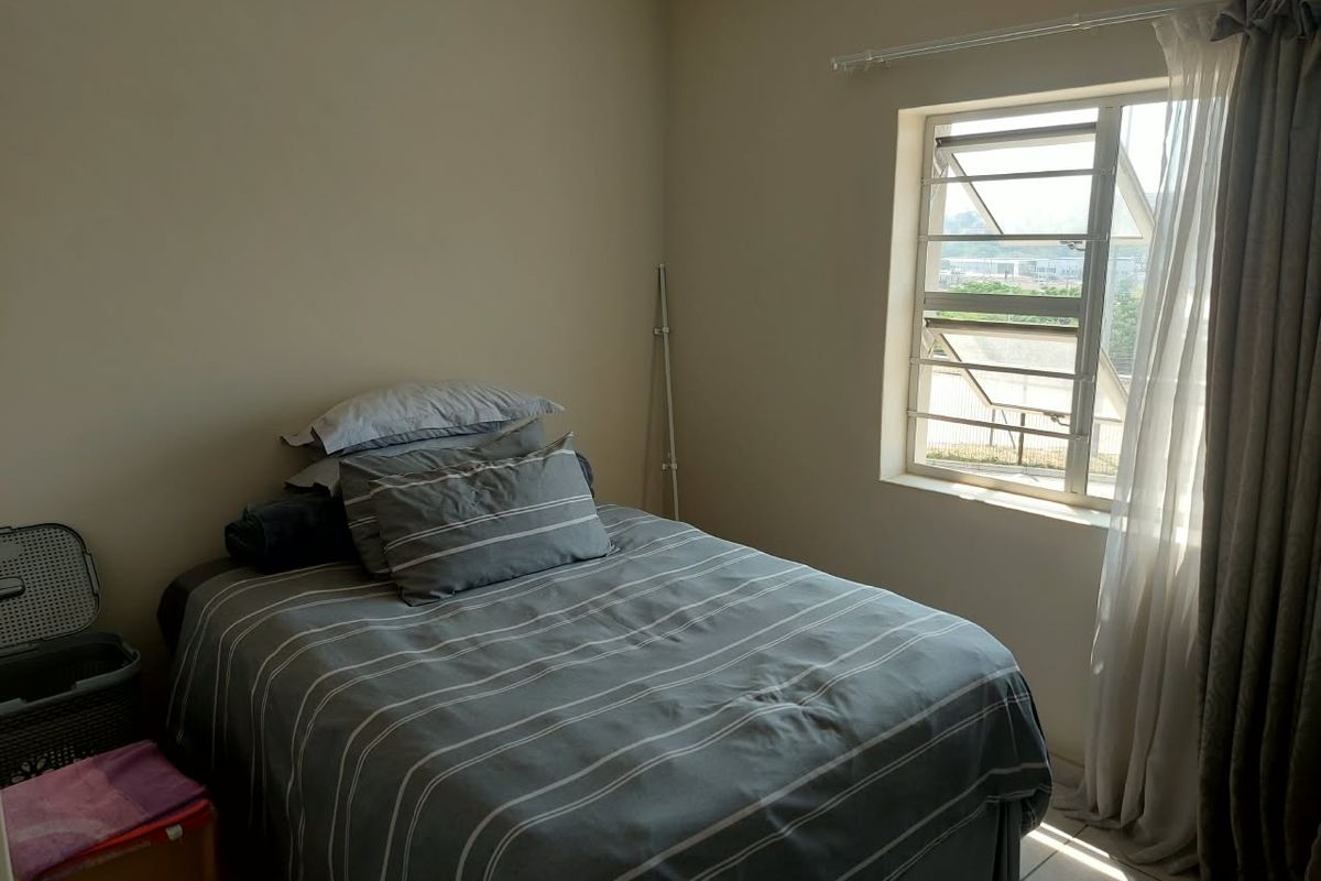 A functional bedroom featuring tiled flooring and a window fitted with security bars, offering natural light and a view of the surrounding area.