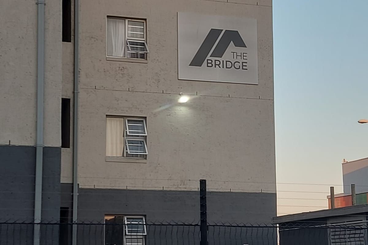 Exterior view of The Bridge apartment complex featuring a multi-story facade with casement windows and security perimeter fencing.
