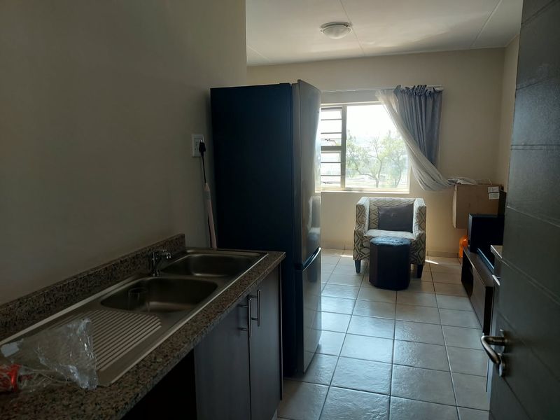 An open-plan kitchen and living area featuring tiled flooring, granite countertops, and a double bowl stainless steel sink with natural light from the window.