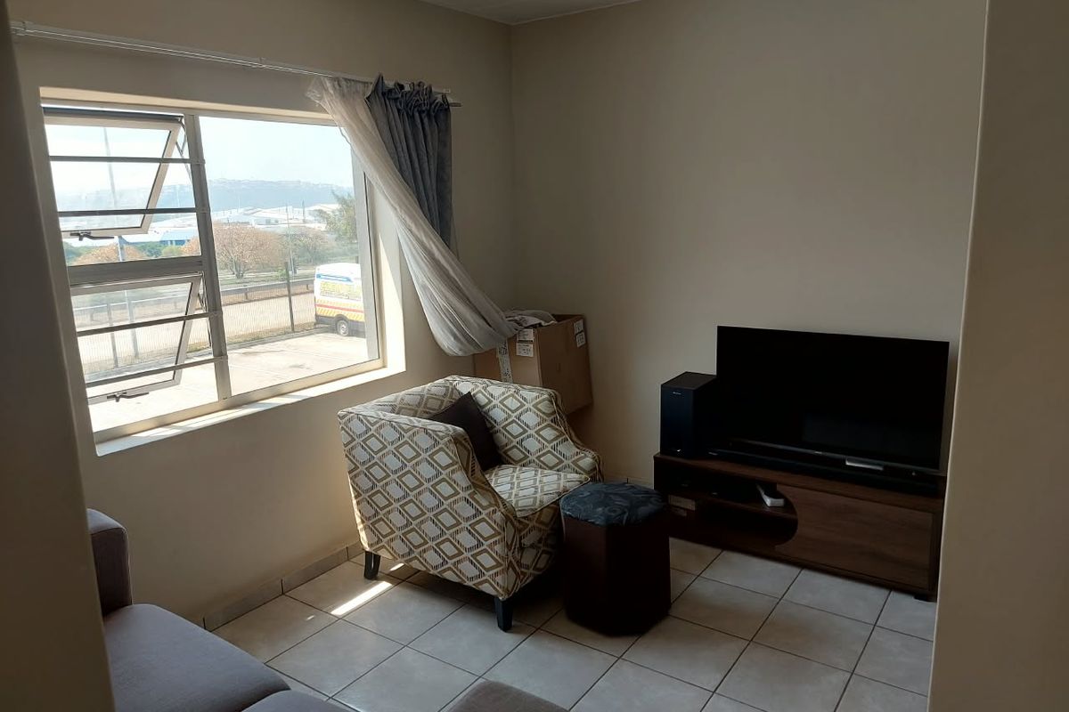A functional living room featuring tiled flooring and a large window providing natural light and exterior views.