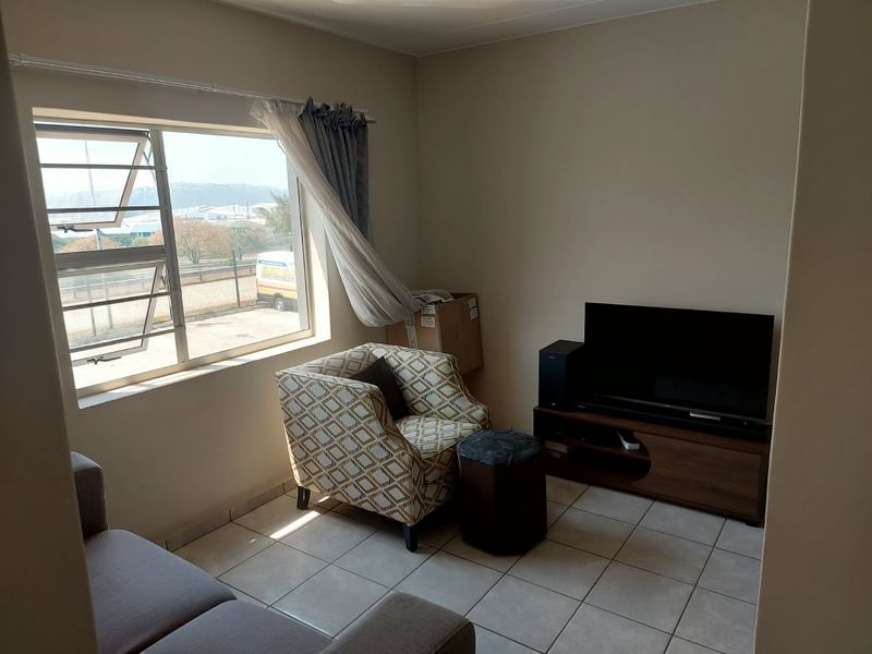 A functional living room featuring tiled flooring and a large window providing natural light and exterior views.