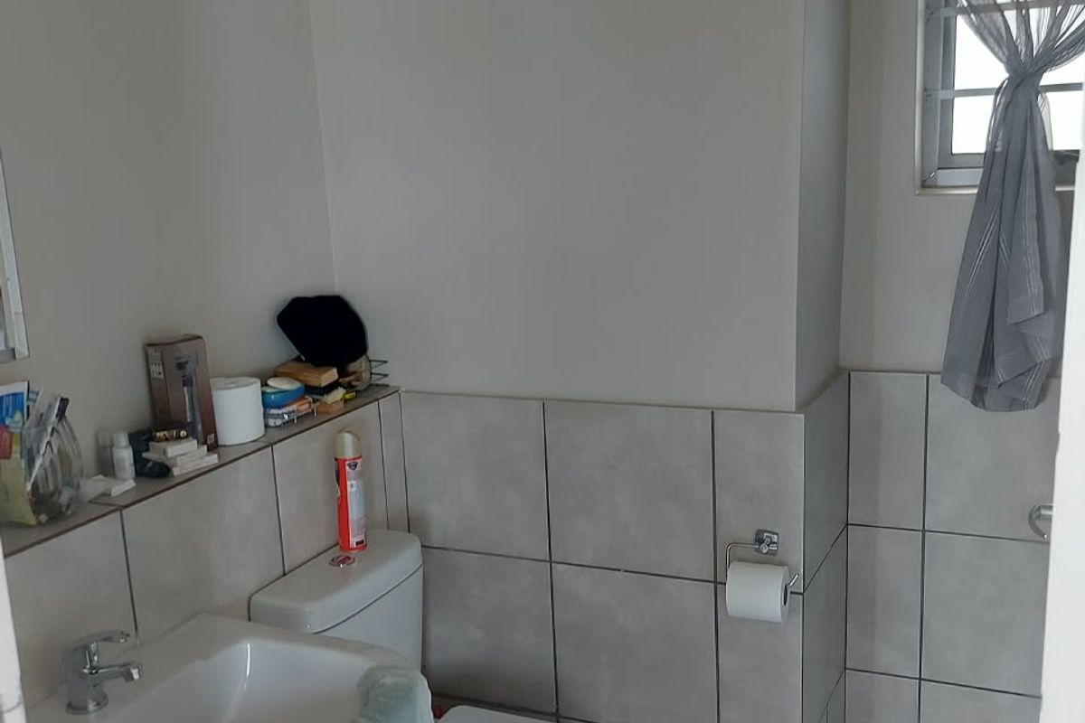 A functional bathroom featuring a pedestal basin, toilet, and neutral wall and floor tiling.