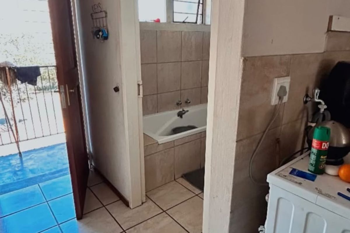 A hallway area featuring tiled flooring, providing direct access to a bathroom with a built-in bathtub and an exterior balcony entrance.