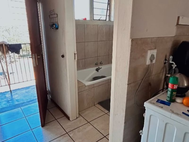 A hallway area featuring tiled flooring, providing direct access to a bathroom with a built-in bathtub and an exterior balcony entrance.