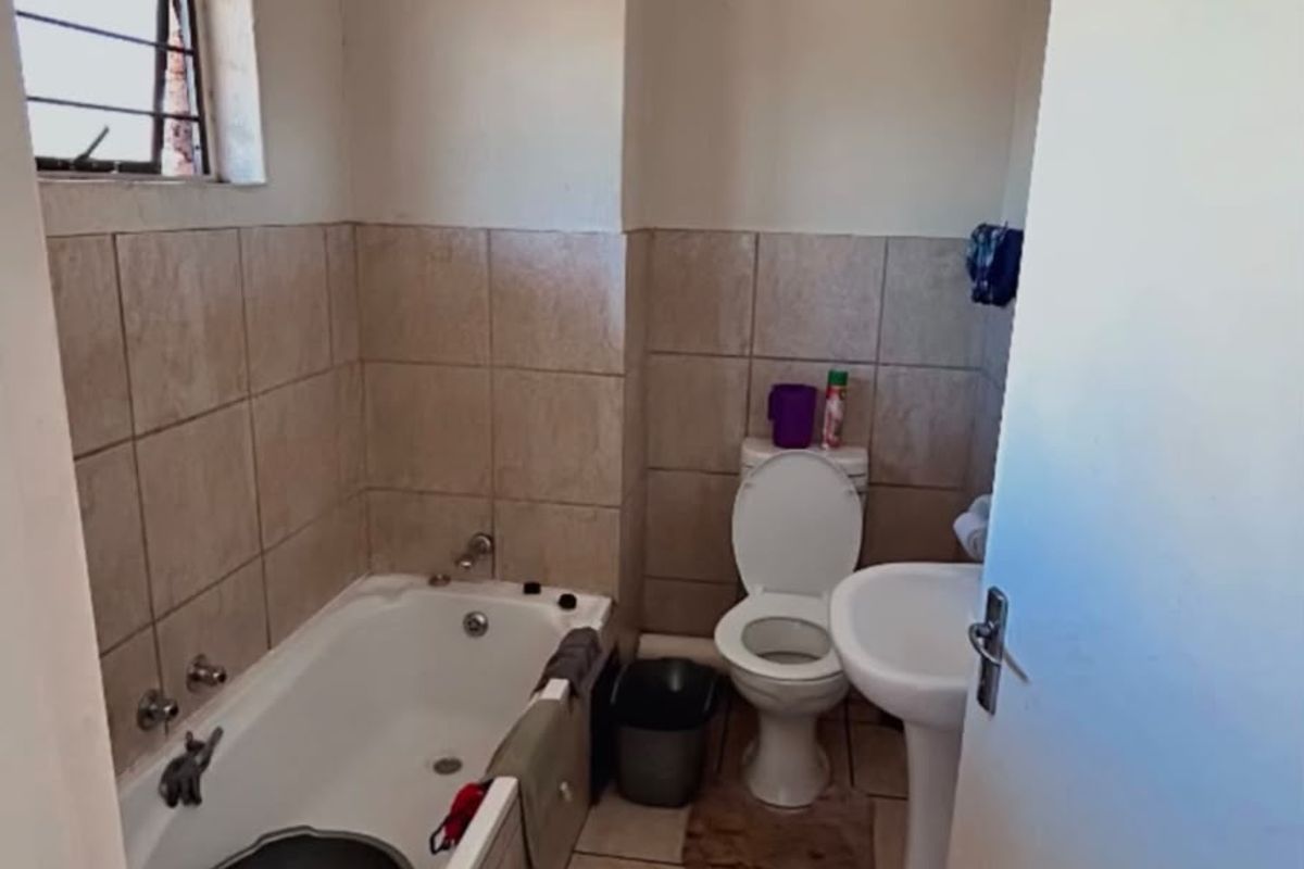 A functional bathroom featuring a bathtub, pedestal basin, and toilet with neutral wall and floor tiling, offering potential for modernization.