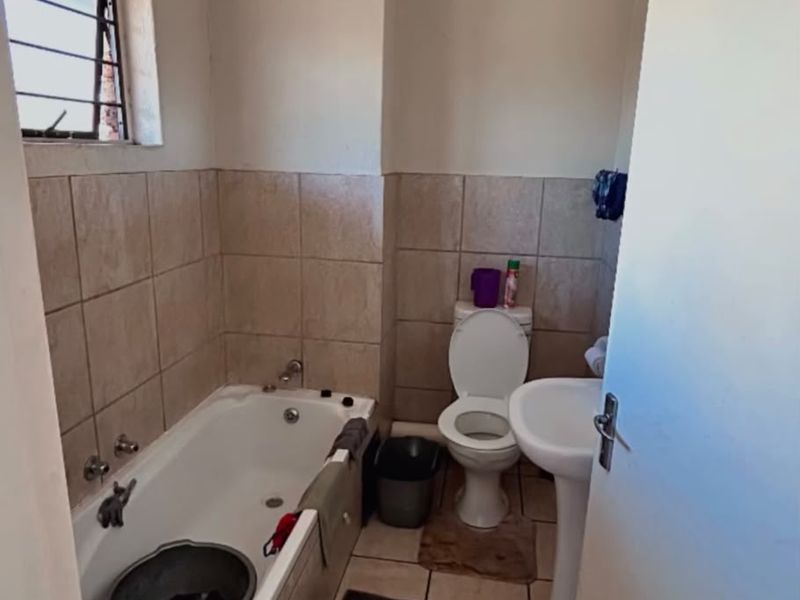 A functional bathroom featuring a bathtub, pedestal basin, and toilet with neutral wall and floor tiling, offering potential for modernization.