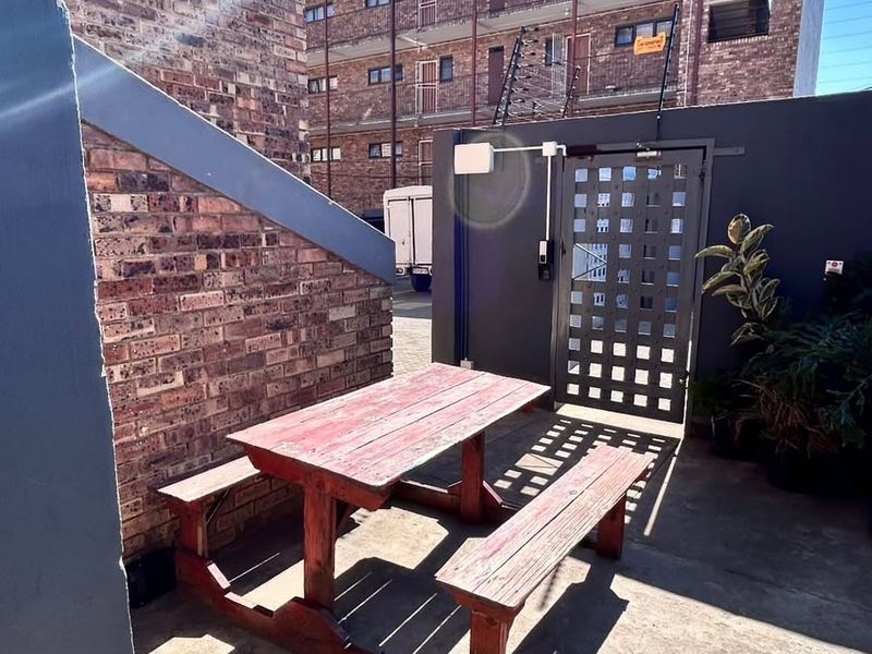 A paved outdoor patio area featuring brick walling, a secure metal gate, and perimeter electric fencing within an apartment complex setting.