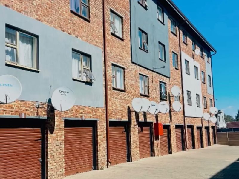 Exterior view of an apartment complex featuring a brick facade, multiple garage units, and paved driveway access.