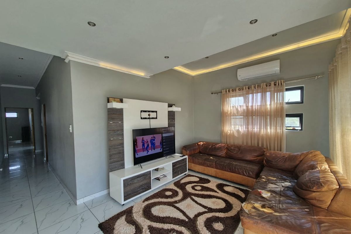 A well-lit living room featuring tiled flooring, recessed ceiling lighting, a built-in media unit, and a wall-mounted air conditioning unit.