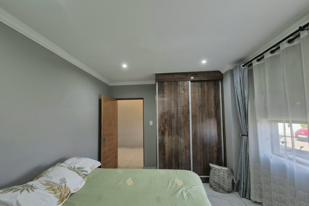 A well-maintained bedroom featuring modern tiled flooring, recessed downlighting, decorative cove cornicing, and a large built-in wardrobe with a wood-grain finish.