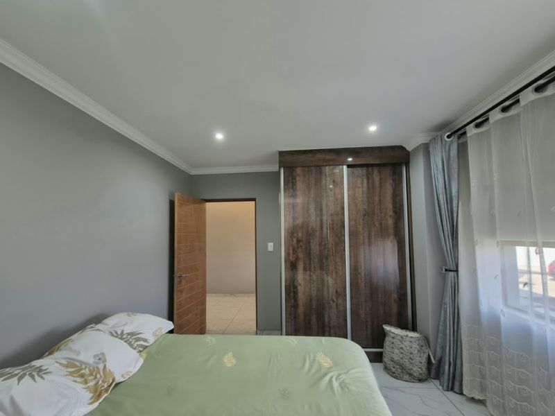 A well-maintained bedroom featuring modern tiled flooring, recessed downlighting, decorative cove cornicing, and a large built-in wardrobe with a wood-grain finish.