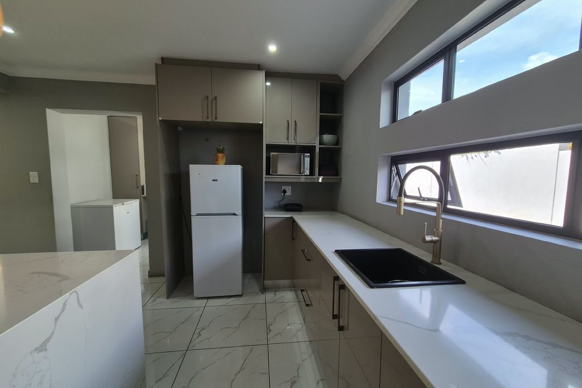 Modern kitchen featuring sleek cabinetry, quartz countertops, a contemporary undermount sink with a gold mixer tap, and polished marble-look floor tiles.