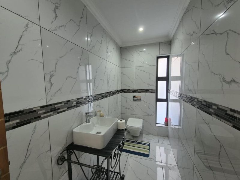 Modern bathroom featuring floor-to-ceiling marble-look tiles, a mosaic accent border, a wall-mounted toilet, and a contemporary vessel sink with chrome fixtures.