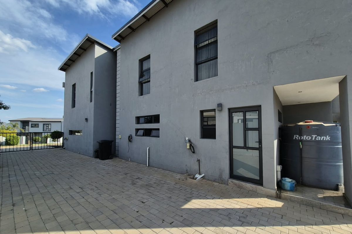 Rear exterior view of the property featuring paved driveway, water storage tank, and modern grey plastered walls with aluminum window frames.