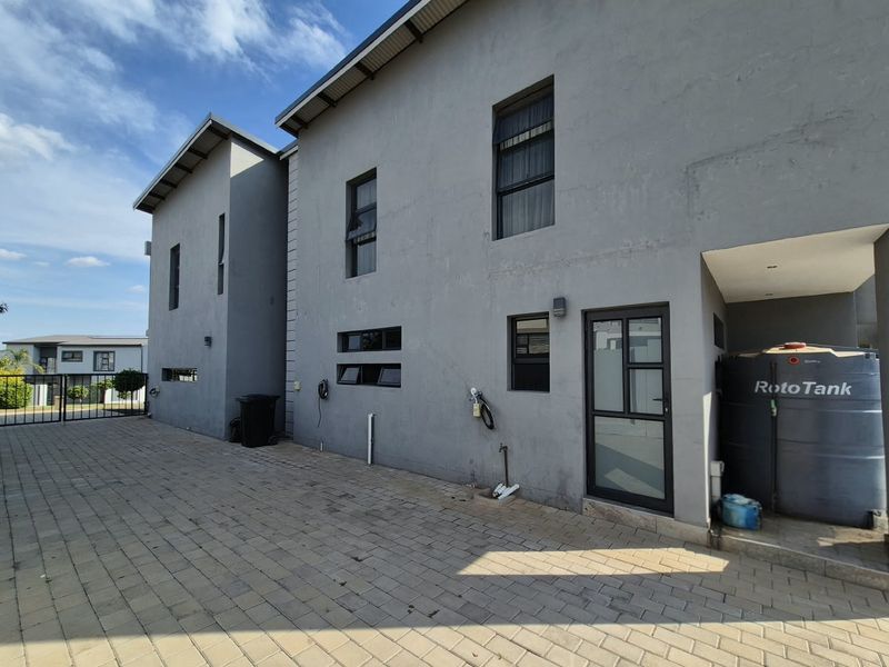 Rear exterior view of the property featuring paved driveway, water storage tank, and modern grey plastered walls with aluminum window frames.
