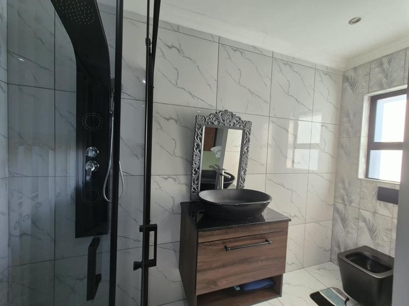 Modern bathroom featuring marble-effect wall tiles, a sleek black shower panel, a wood-finish vanity with a vessel sink, and a wall-mounted toilet.