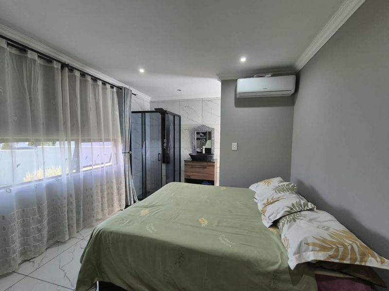 A modern bedroom featuring an open-plan en-suite shower, vanity with vessel sink, air conditioning, and sleek tiled flooring.