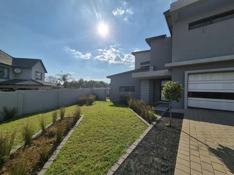 Modern front elevation featuring a paved driveway, sectional garage door, and a well-maintained landscaped garden with a secure boundary wall.