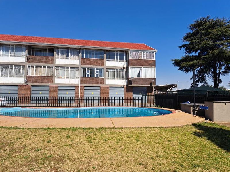 Exterior view of an apartment complex featuring a communal swimming pool, paved deck area, and ground-level garage units.