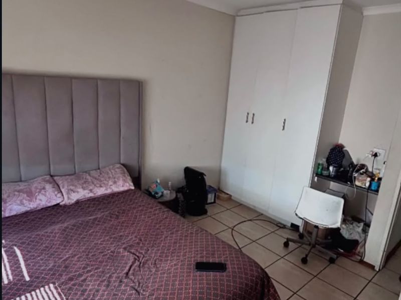 A bedroom featuring tiled flooring, a built-in wardrobe, and a ceiling light fixture, offering a functional space with potential for cosmetic updates.