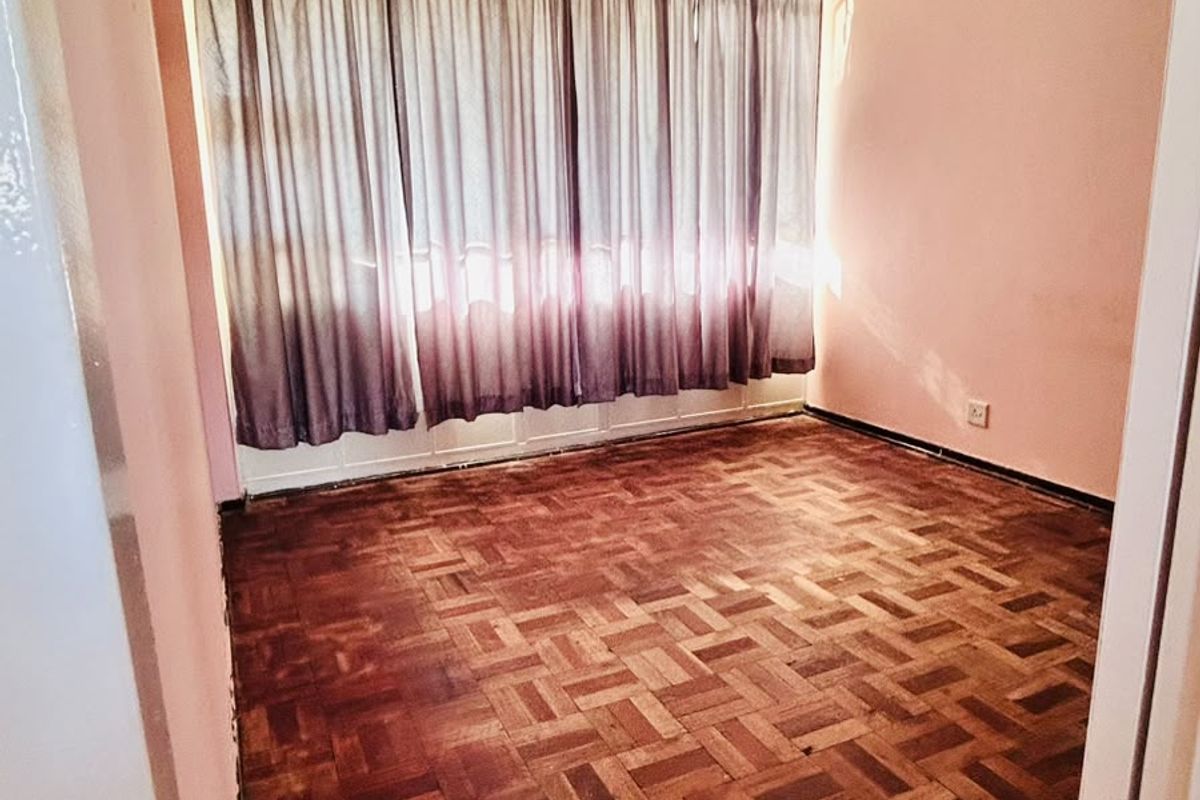 An empty bedroom featuring traditional parquet flooring and a large window with curtains, offering a blank canvas for renovation or interior design.