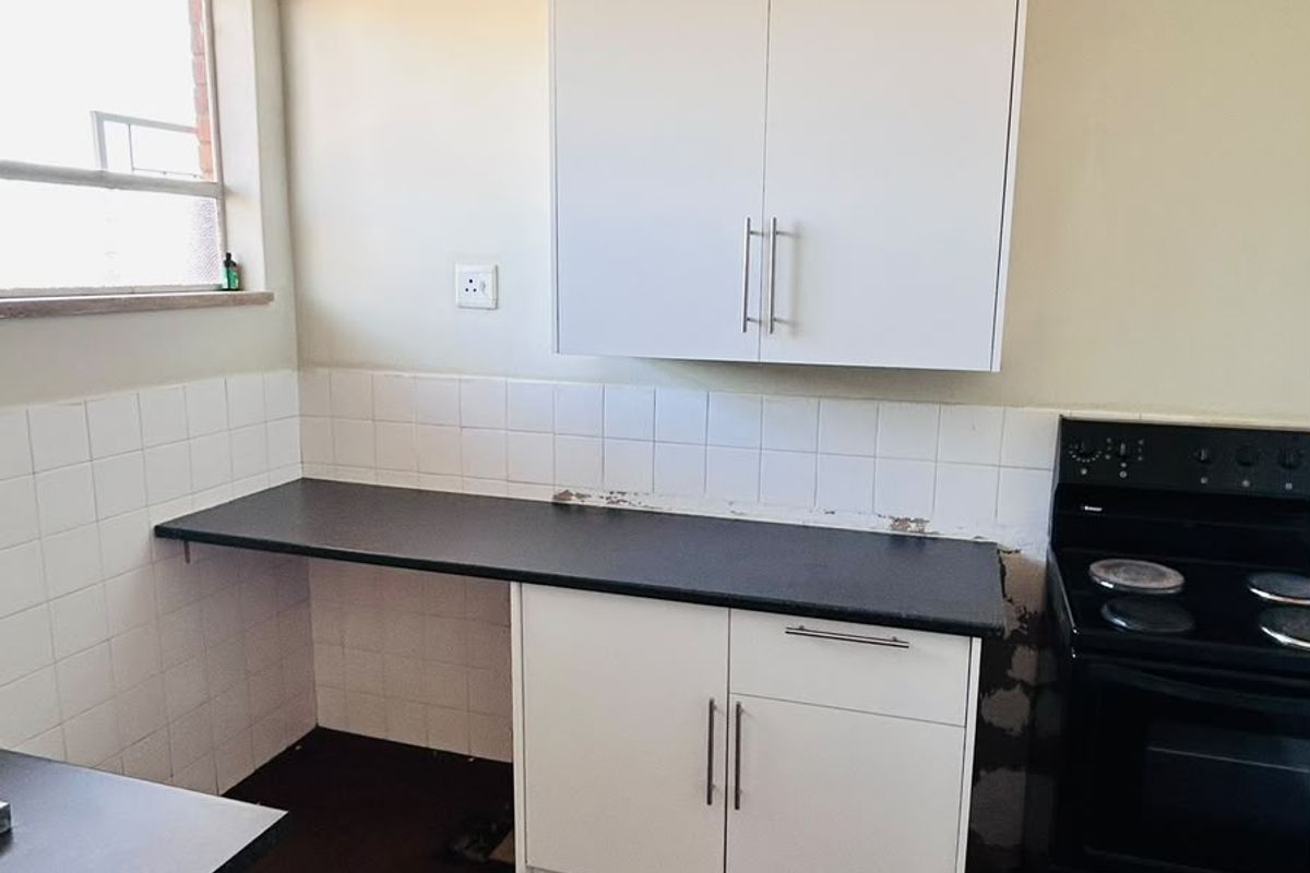 A functional kitchen area featuring white cabinetry, dark countertops, and a tiled backsplash, requiring some cosmetic updates to the wall finishes and flooring.