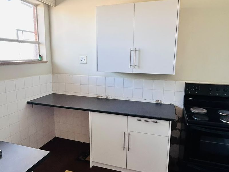 A functional kitchen area featuring white cabinetry, dark countertops, and a tiled backsplash, requiring some cosmetic updates to the wall finishes and flooring.
