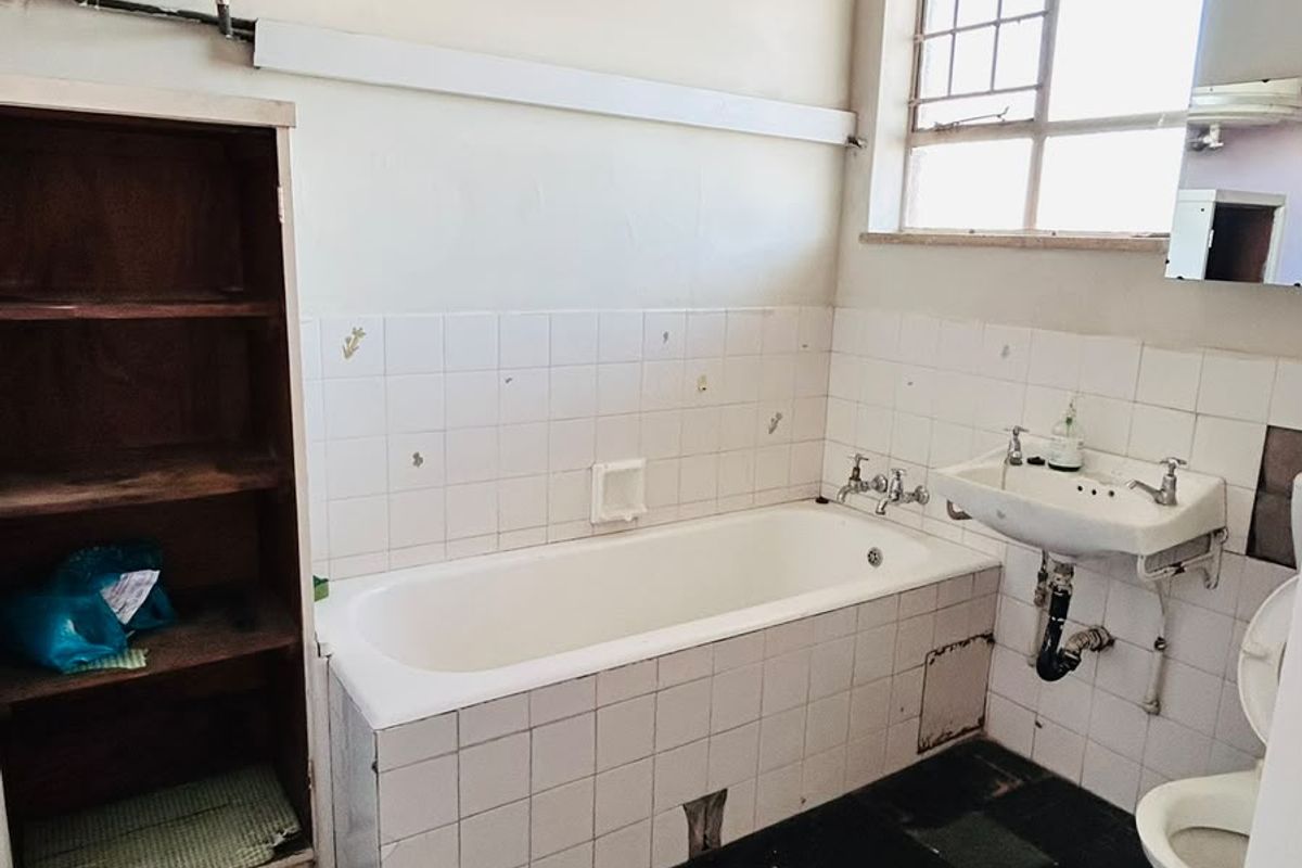 A dated bathroom featuring a bathtub, wall-mounted basin, toilet, and built-in shelving, requiring significant renovation and modernization of finishes.