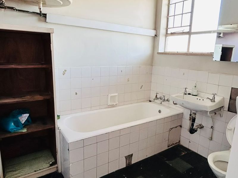 A dated bathroom featuring a bathtub, wall-mounted basin, toilet, and built-in shelving, requiring significant renovation and modernization of finishes.
