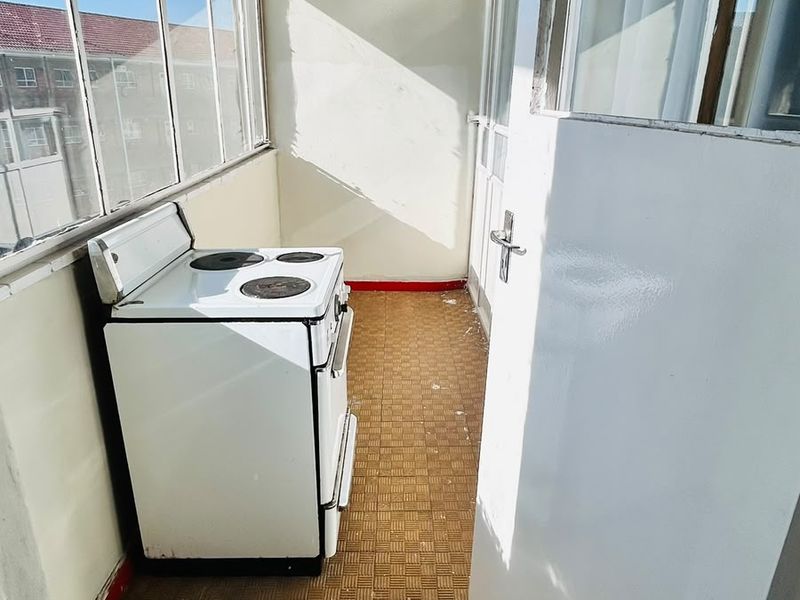 A narrow, sunlit utility or scullery area featuring tiled flooring, large windows, and a freestanding electric stove.