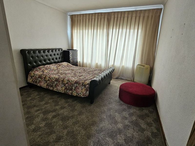 A bedroom featuring carpeted flooring and full-length window curtains, requiring cosmetic updates to the wall surfaces and flooring to enhance its appeal.