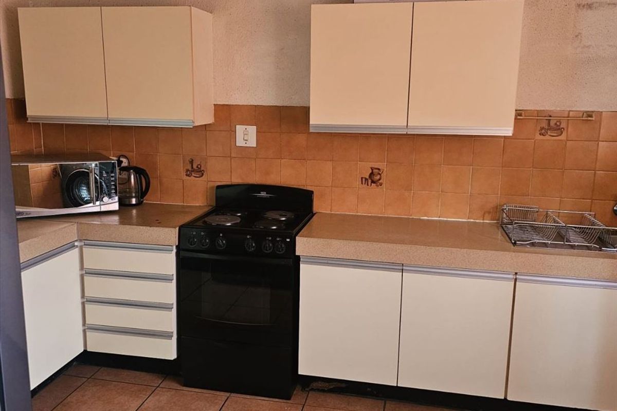 A functional kitchen featuring dated cabinetry, laminate countertops, and ceramic tile finishes, offering potential for a modern renovation.