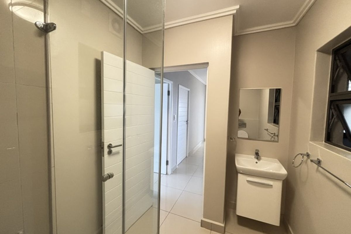 A clean and modern bathroom featuring a glass shower enclosure, a wall-mounted vanity with basin, and neutral tiled flooring.