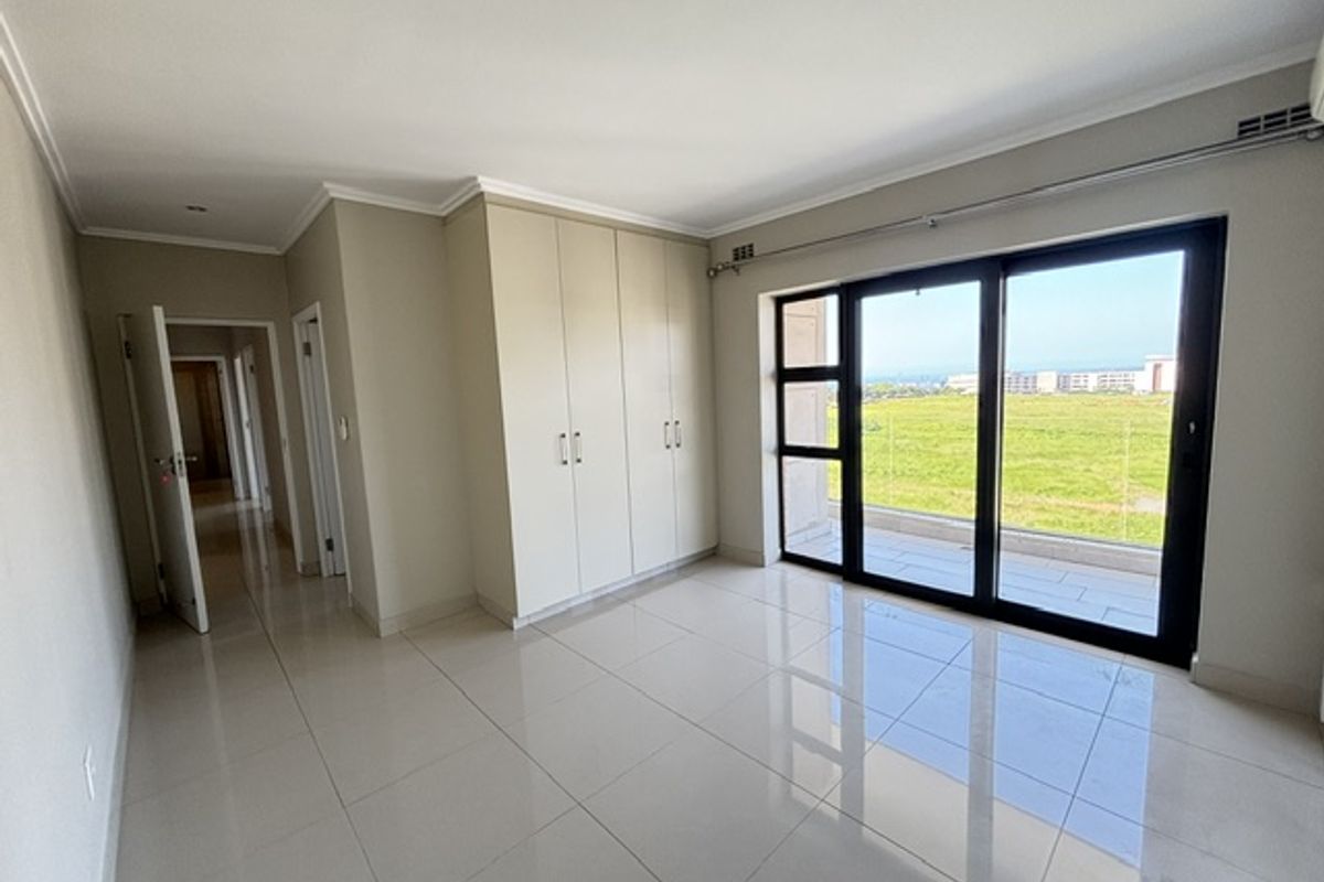 A bright, empty bedroom featuring neutral tiled flooring, ample built-in cupboard space, and large sliding glass doors leading to an outdoor area.