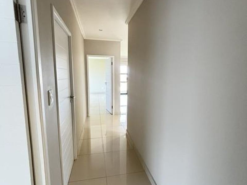 A clean, well-maintained hallway featuring neutral wall tones, polished floor tiles, and recessed lighting, providing access to multiple rooms within the apartment.